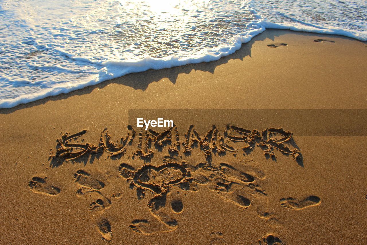 Text and footprints on sand by surf at beach during sunset