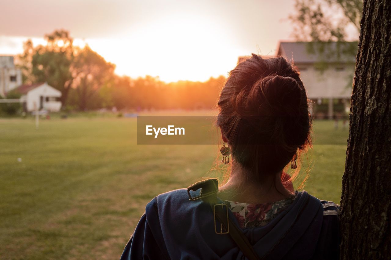 Rear view of woman standing by tree at park during sunset