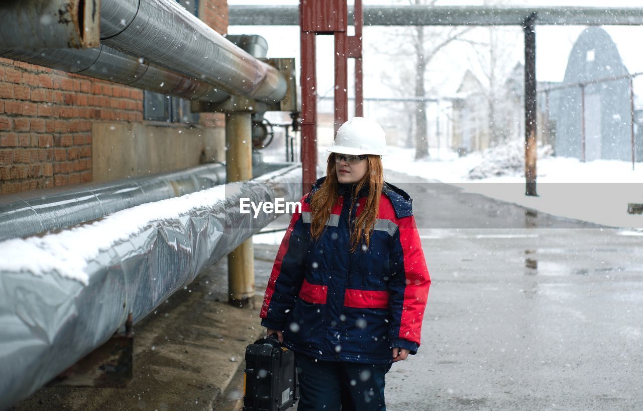 Young woman worker standing in snow in an industrial area