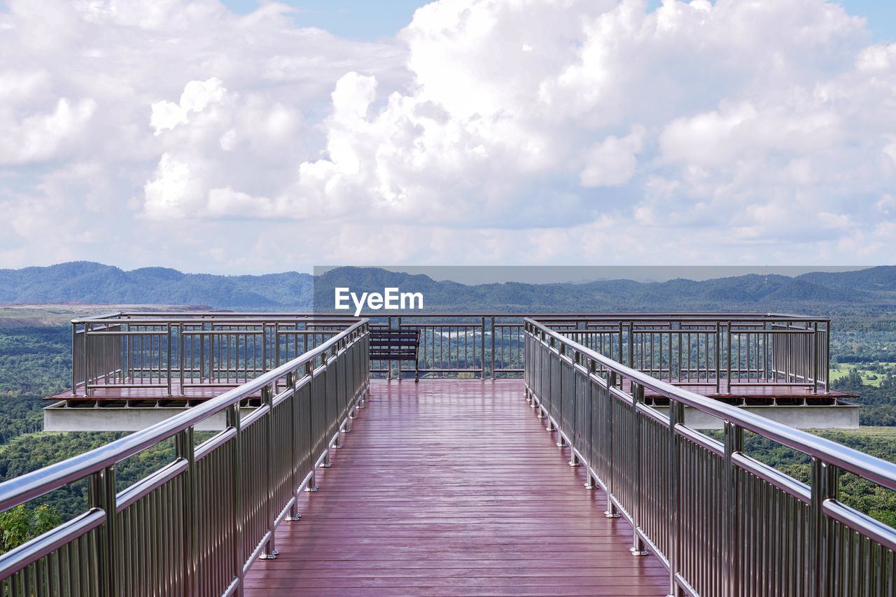 FOOTBRIDGE OVER LAKE AGAINST CLOUDY SKY