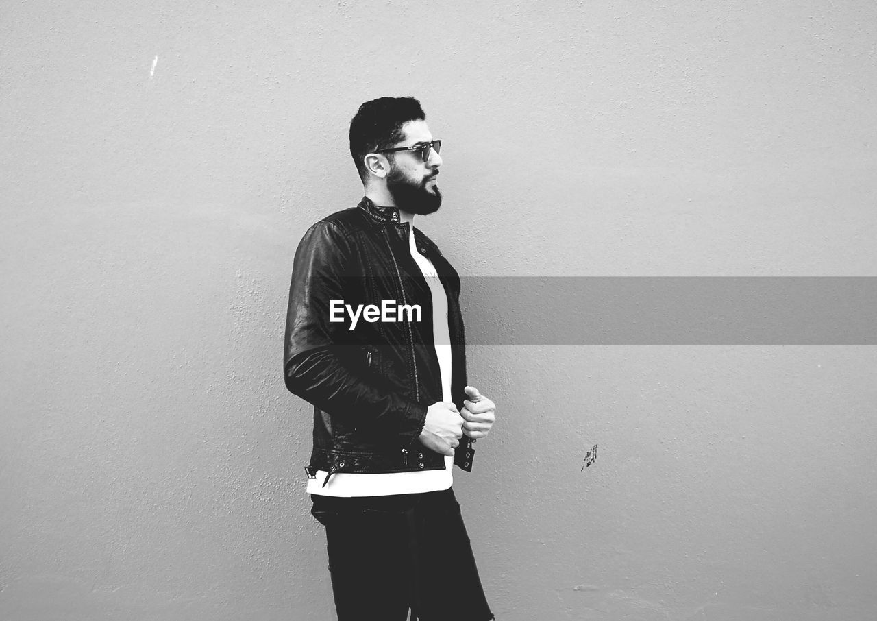 Side view of handsome man looking away while standing against wall