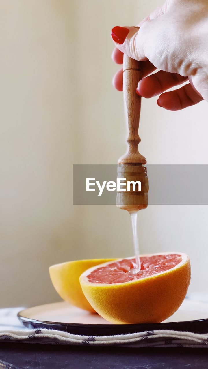 Cropped hand pouring honey on grapefruit