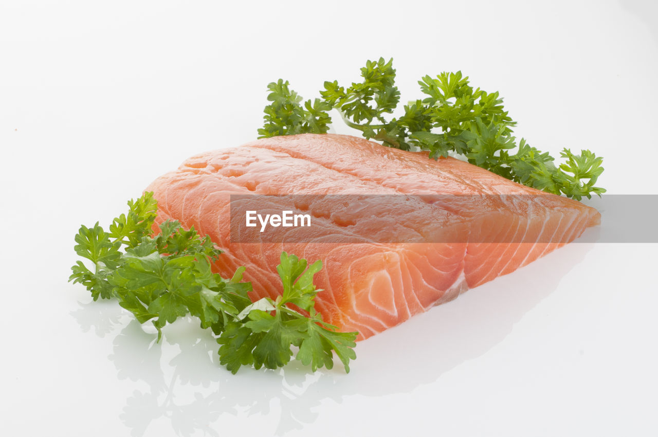 Close-up of raw seafood with herb over white background