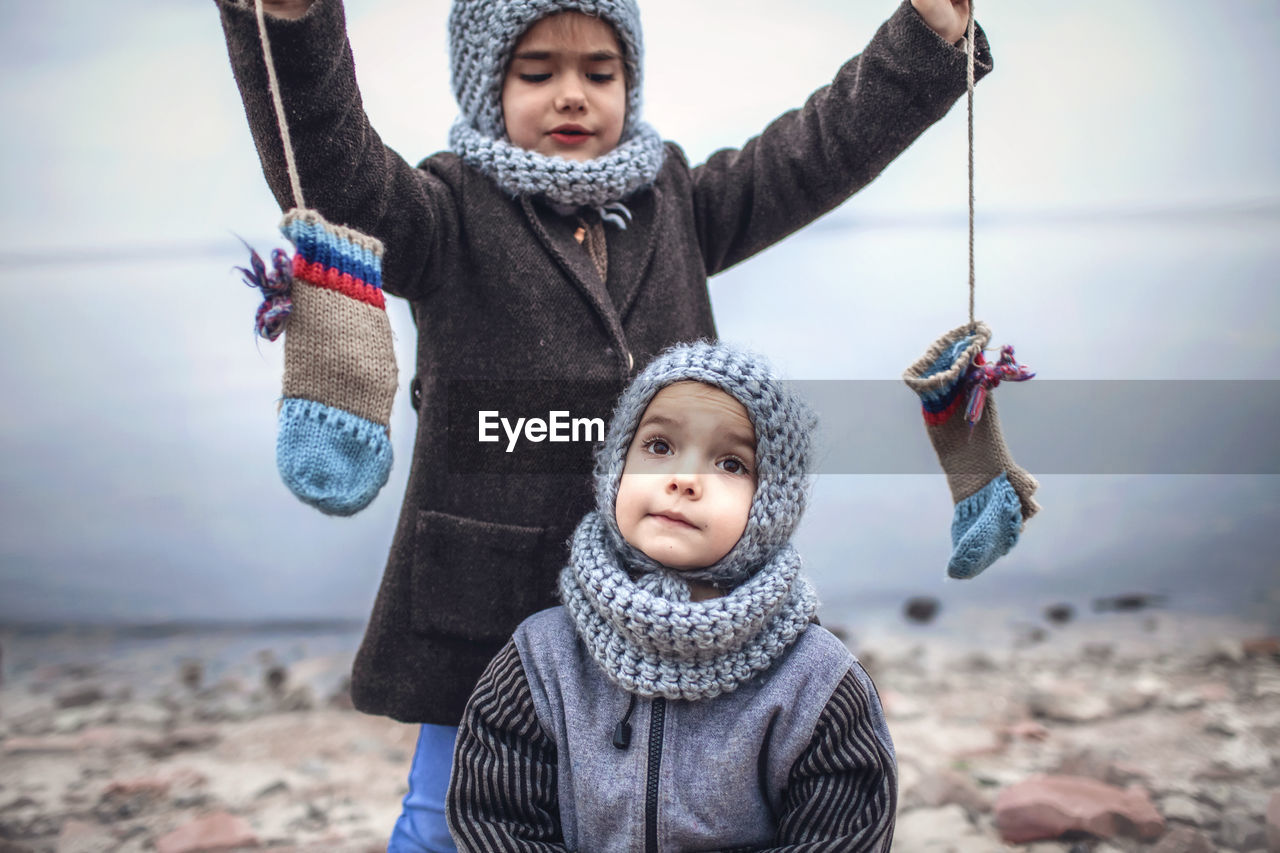 Girl in knitted grey hat sharing gloves with her frozen brother