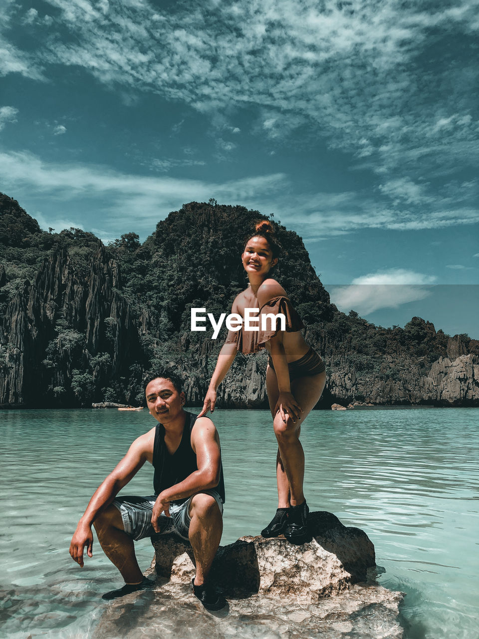 Young couple sitting on rock by sea against sky