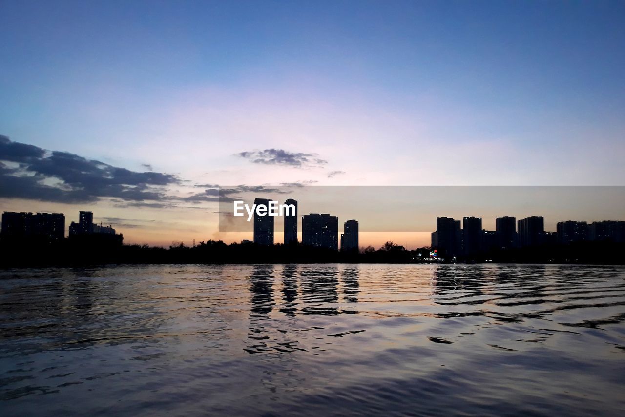 CITY BUILDINGS BY SEA AGAINST SKY DURING SUNSET