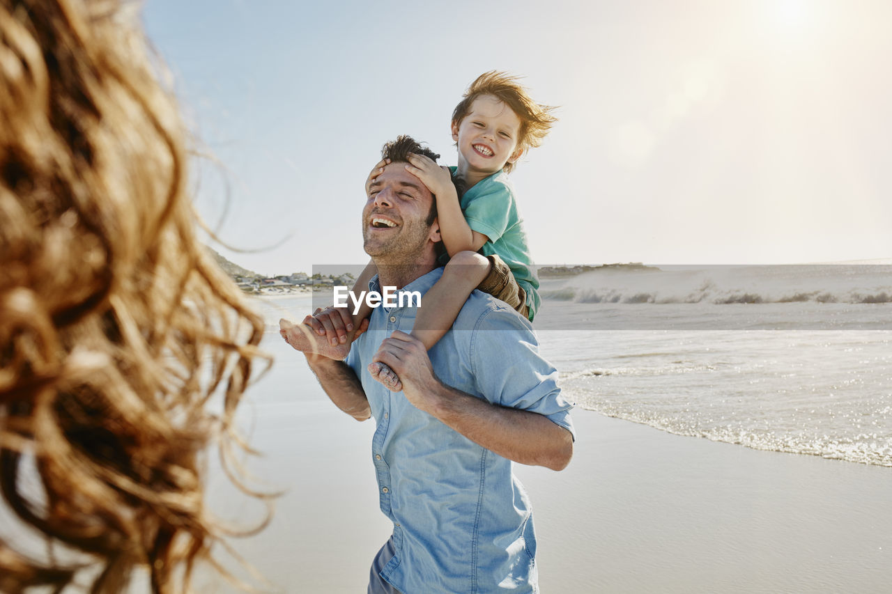 Father carrying his little son on shoulders on the beach