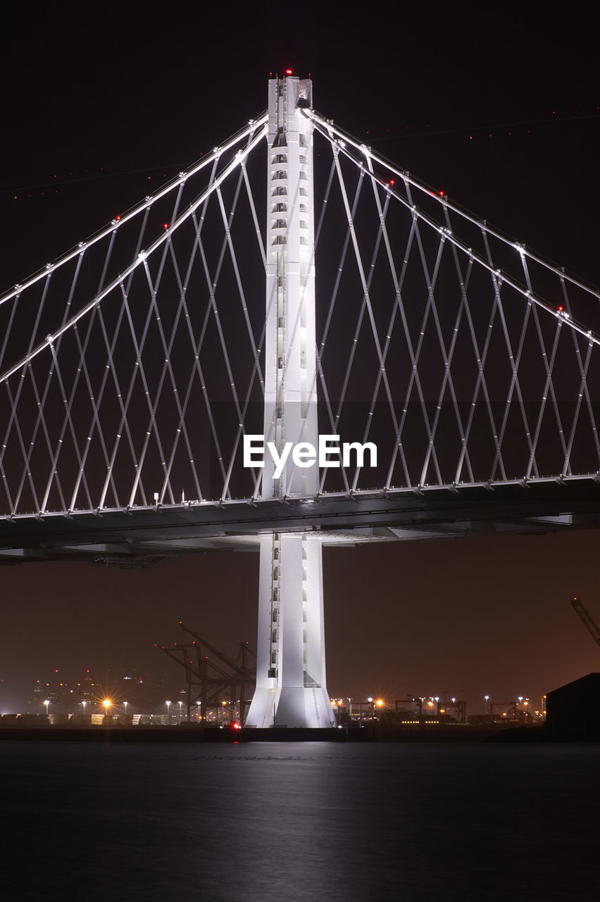 VIEW OF SUSPENSION BRIDGE OVER RIVER AT NIGHT