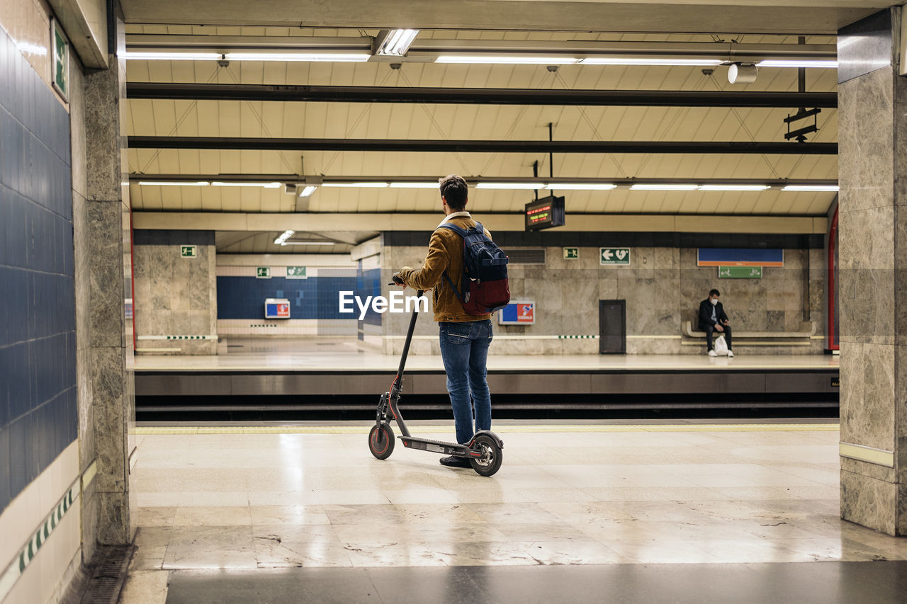 Man in stylish outfit waiting for the metro with electric scooter in the underground
