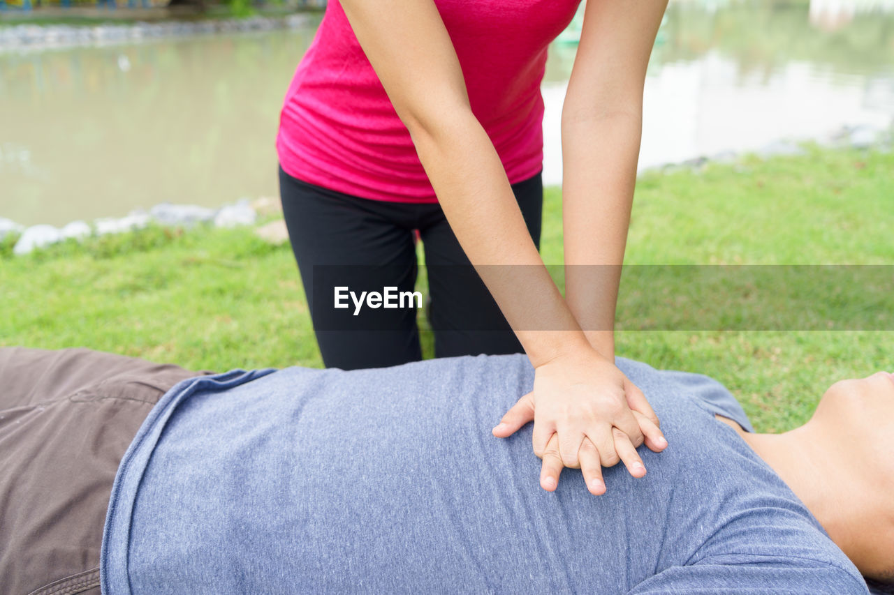 Midsection of woman giving cpr to man lying in grassy field