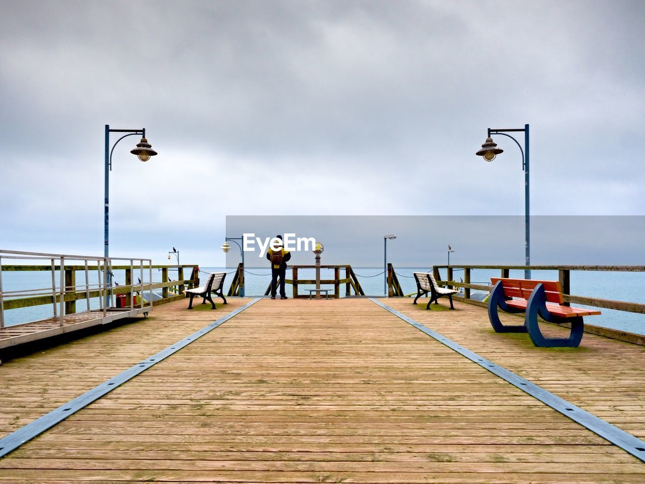 Man on long touristic mole within autumn misty morning. tourist at handrail. wet wooden board