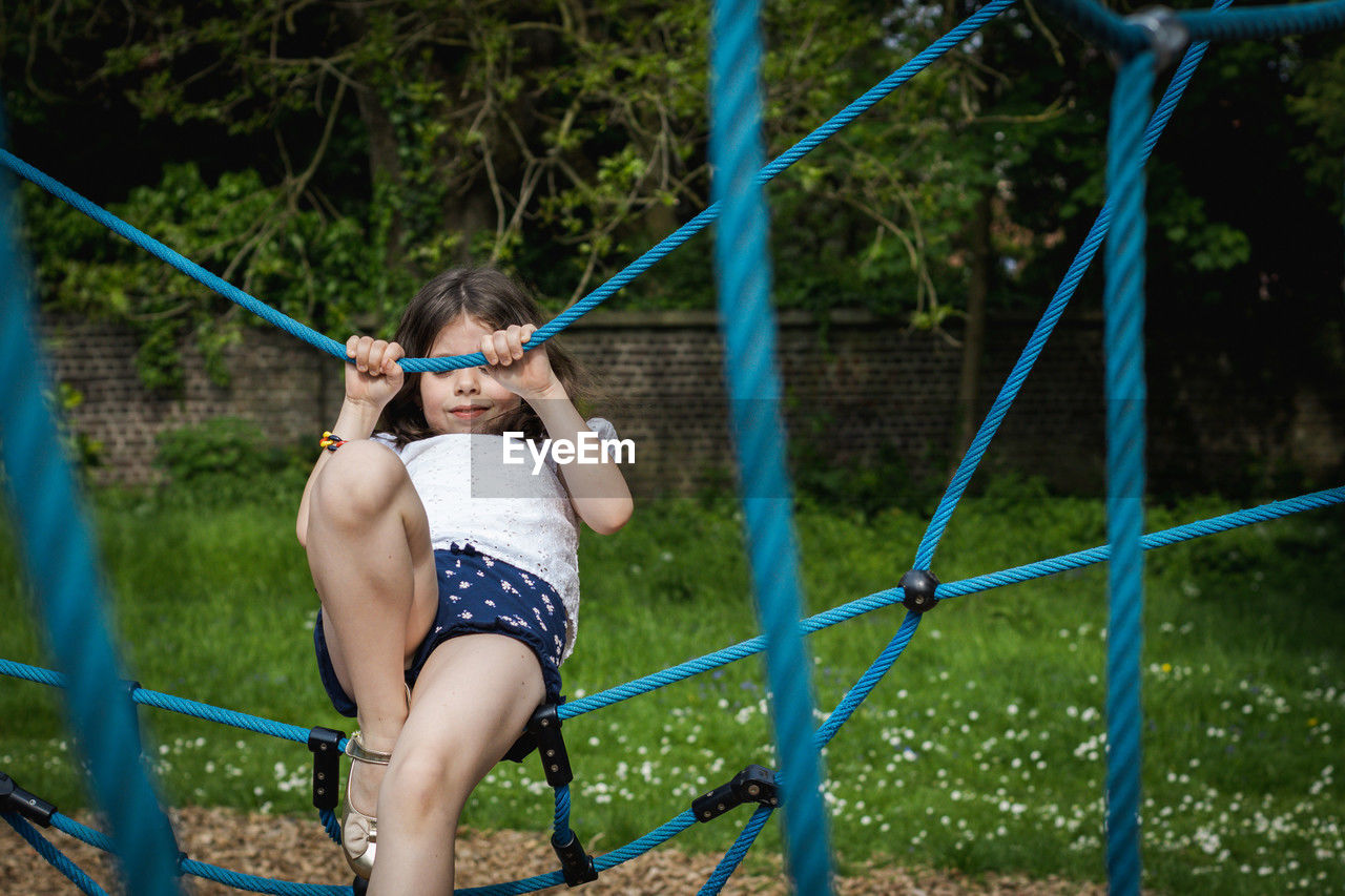 A girl climbs a rope swing in the park.