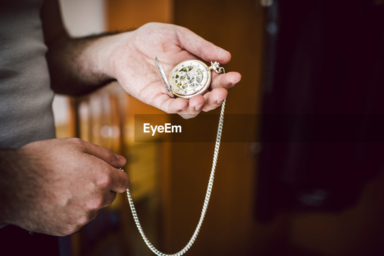 Midsection of man holding pocket watch at home