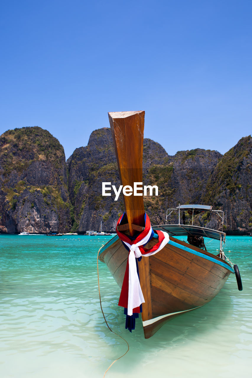 Longtail boat moored in sea against clear blue sky