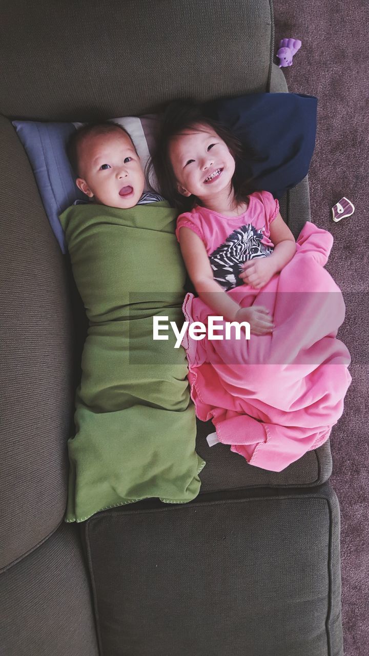 Directly above view of baby boy lying by sister on sofa at home