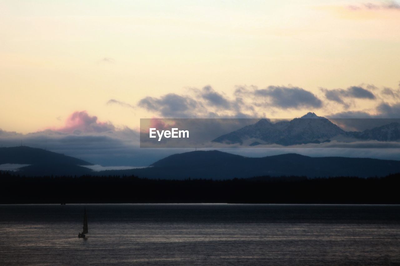 Silhouette of sailboat in sea against cloudy sky