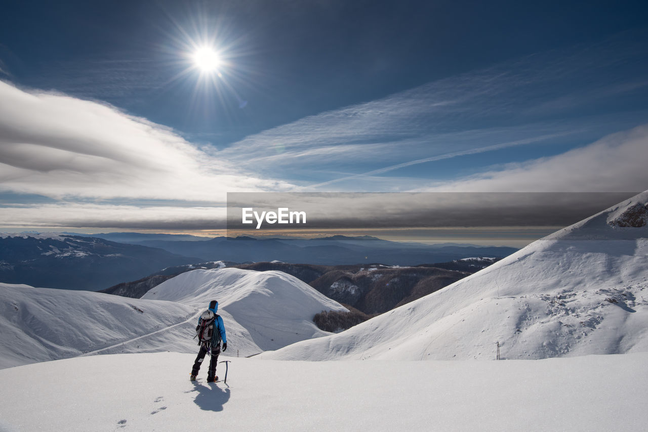 WOMAN WALKING ON SNOWCAPPED MOUNTAIN AGAINST SKY