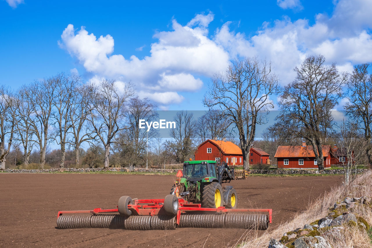 sky, field, tree, cloud, nature, plant, rural area, farm, soil, agriculture, landscape, construction industry, architecture, blue, transportation, vehicle, day, environment, outdoors, machinery, agricultural machinery, no people, industry, playground, built structure, bare tree, rural scene, occupation, land