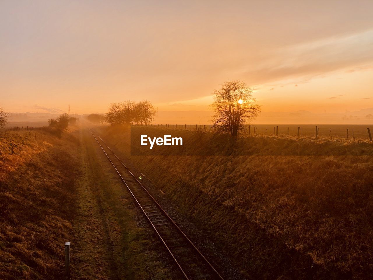 Railroad tracks on field against sky during sunset