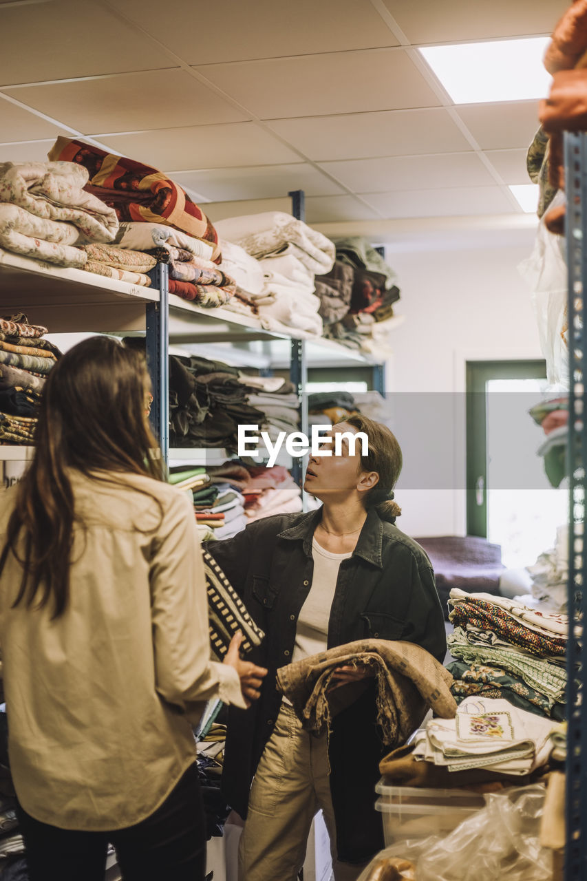 Female fashion designers talking while standing near rack at workshop