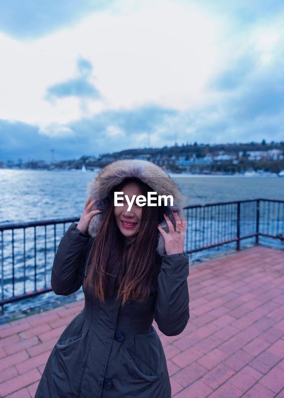 Portrait of beautiful young woman against river