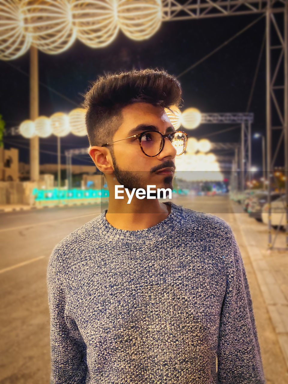 Young man looking away while standing on illuminated road