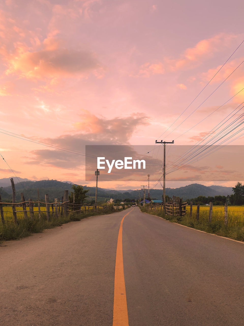 ROAD BY ELECTRICITY PYLONS AGAINST SKY DURING SUNSET