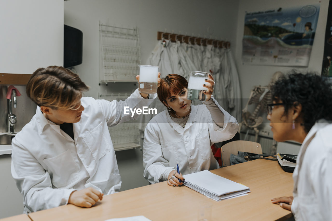 Students and teacher examining chemical in beaker at school laboratory