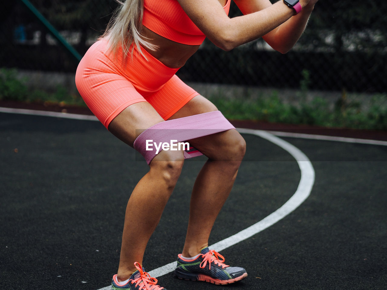 Young beautiful blond fitness model with long hair in neon orange activewear doing squats exercise
