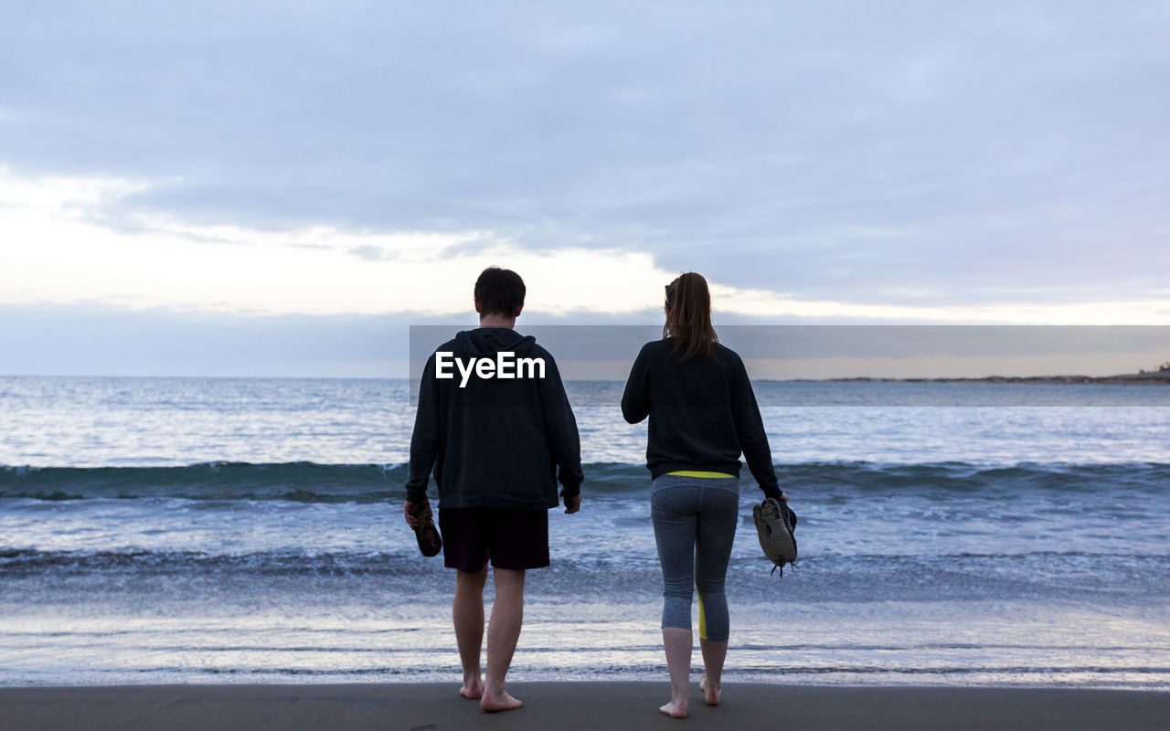 Rear view of people walking at beach against sky