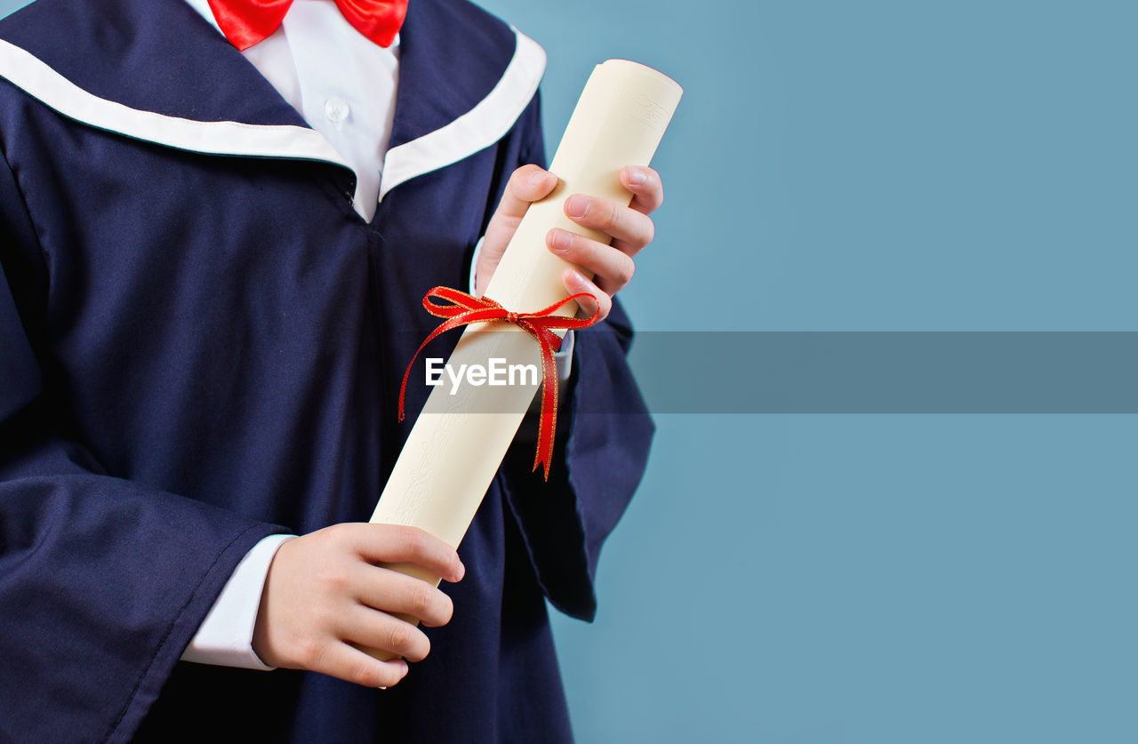 Midsection of man holding certificate while standing against blue background