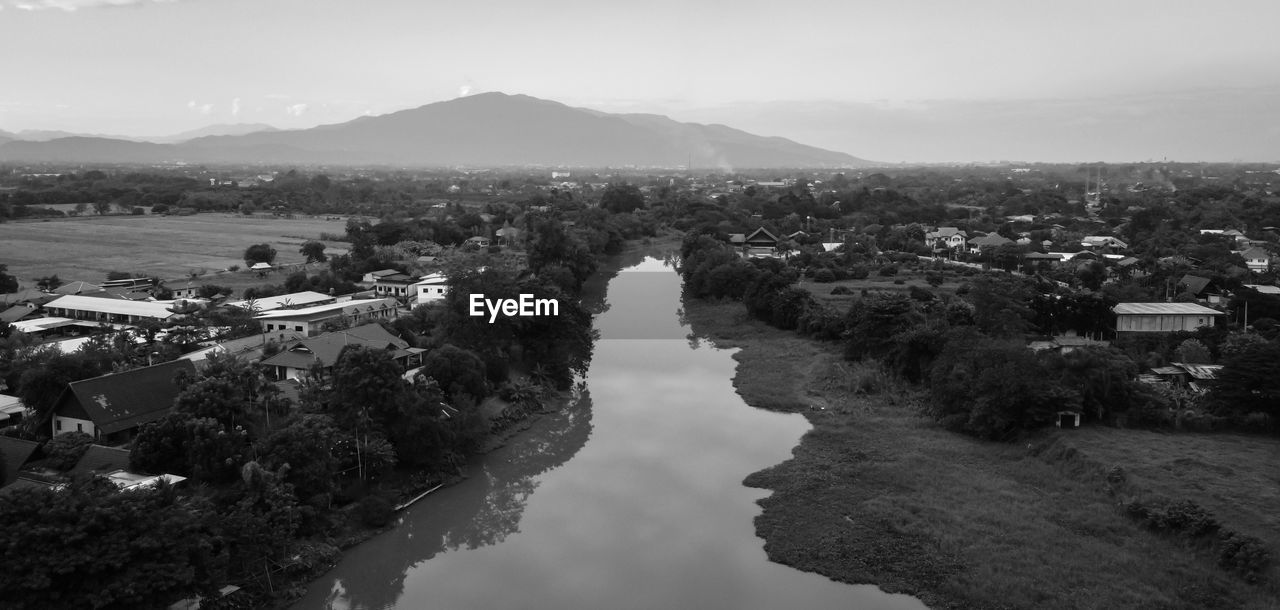 HIGH ANGLE VIEW OF RIVER AMIDST TOWN AGAINST SKY