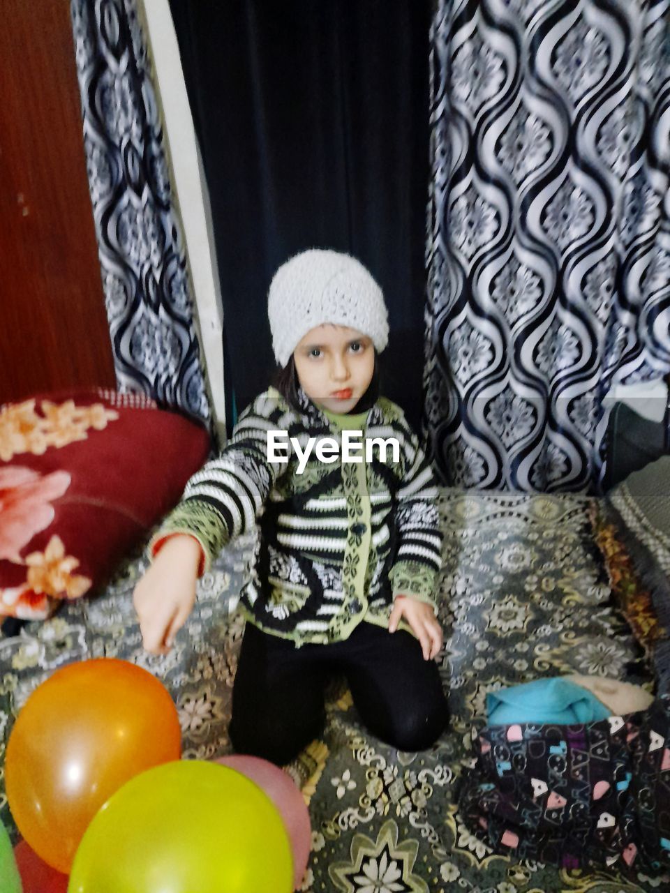 childhood, child, one person, indoors, innocence, full length, sitting, portrait, clothing, front view, looking at camera, men, baby, toddler, cute, toy, domestic room, home interior, casual clothing, hat, celebration, balloon, lifestyles, emotion, person, looking, furniture, carpet, happiness, multi colored, three quarter length