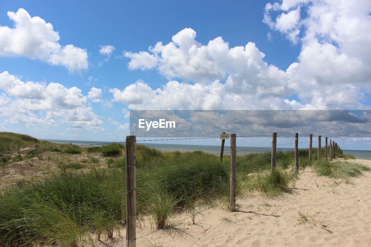 Fence on sand with grass by sea