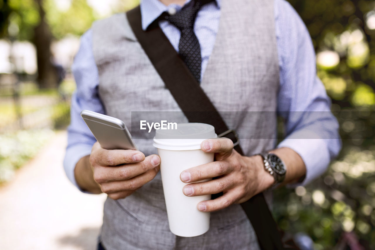 Close-up of businessman with coffee and smartphone in city park