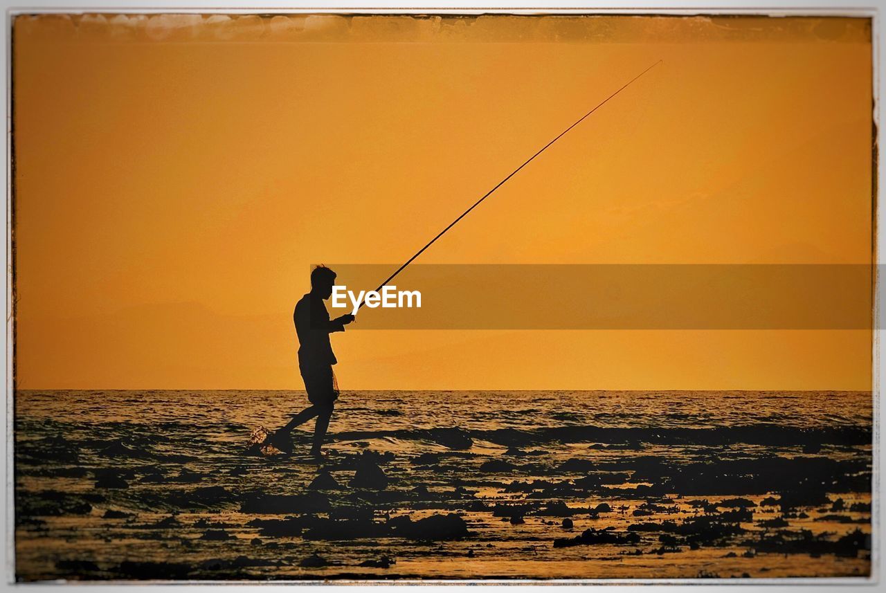 SILHOUETTE MAN FISHING ON SEA AGAINST SKY DURING SUNSET