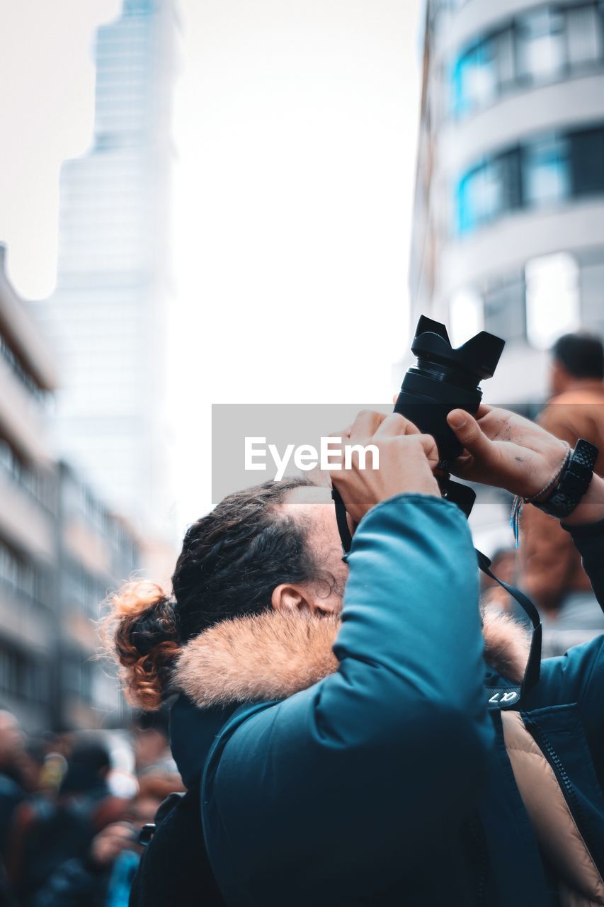 PORTRAIT OF MAN PHOTOGRAPHING AGAINST CITY