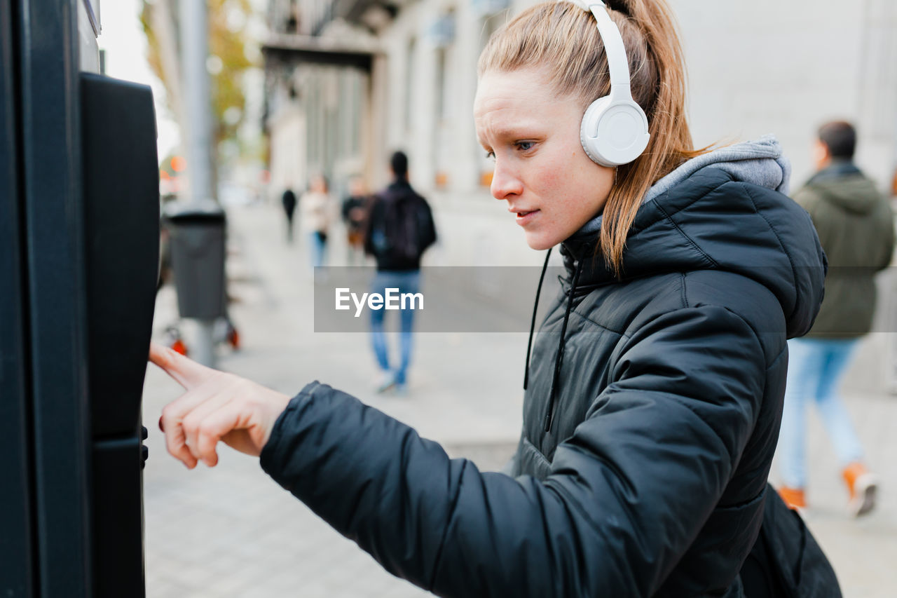 Young woman listening to music using parking meter