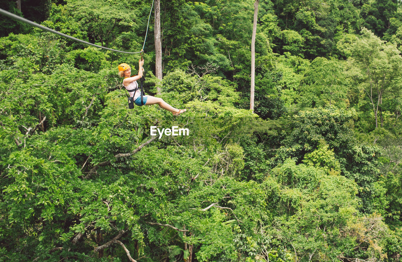 Full length of woman zip lining in forest