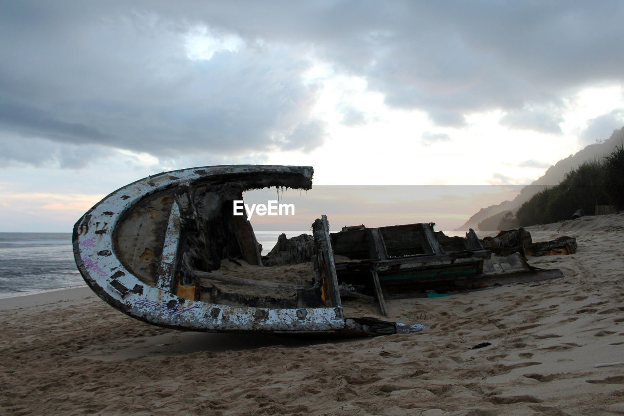 ABANDONED BOAT ON BEACH AGAINST SKY