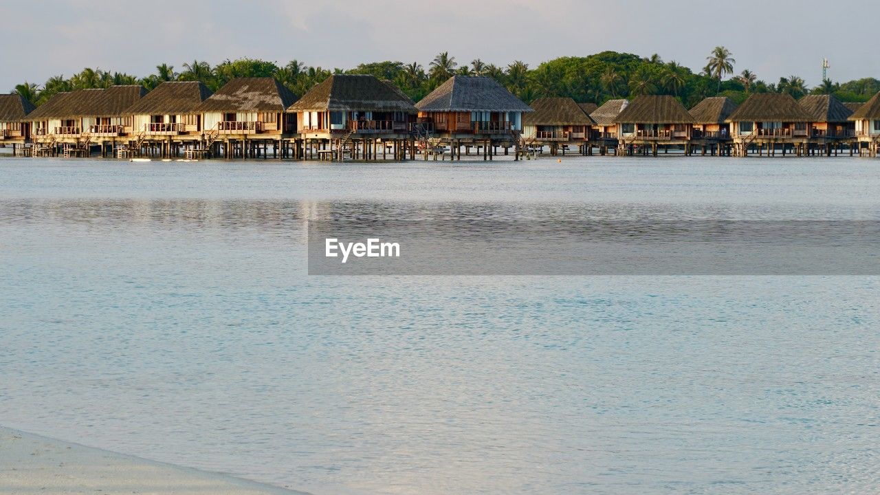 water, architecture, shore, beach, sea, built structure, building exterior, building, land, house, body of water, coast, sky, nature, vacation, travel destinations, residential district, bay, city, ocean, beauty in nature, landscape, tourism, travel, scenics - nature, environment, stilt house, coastline, outdoors, no people, tropical climate, trip, cloud, day, tranquility, sand, holiday, hut, idyllic, village, palm tree, tree, tourist resort, tranquil scene, water's edge, blue, town, pier, waterfront