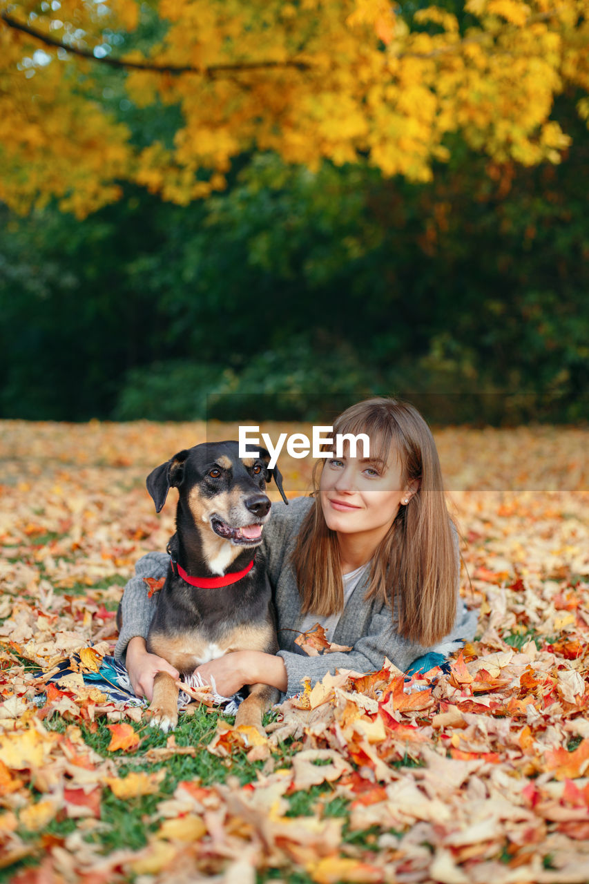 Portrait of woman with dog lying on dry leaves at park during autumn