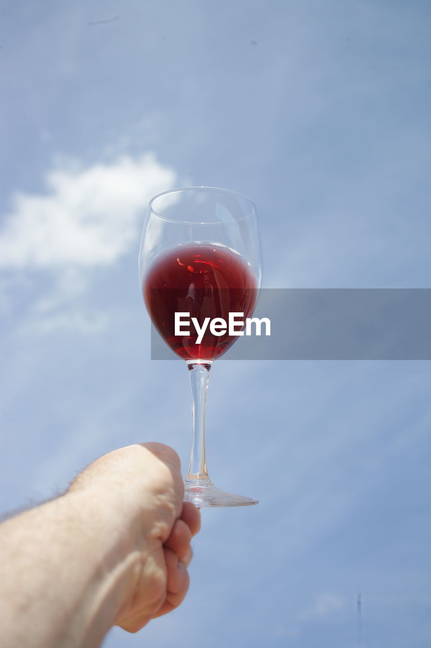 MIDSECTION OF PERSON HOLDING DRINK AGAINST SKY