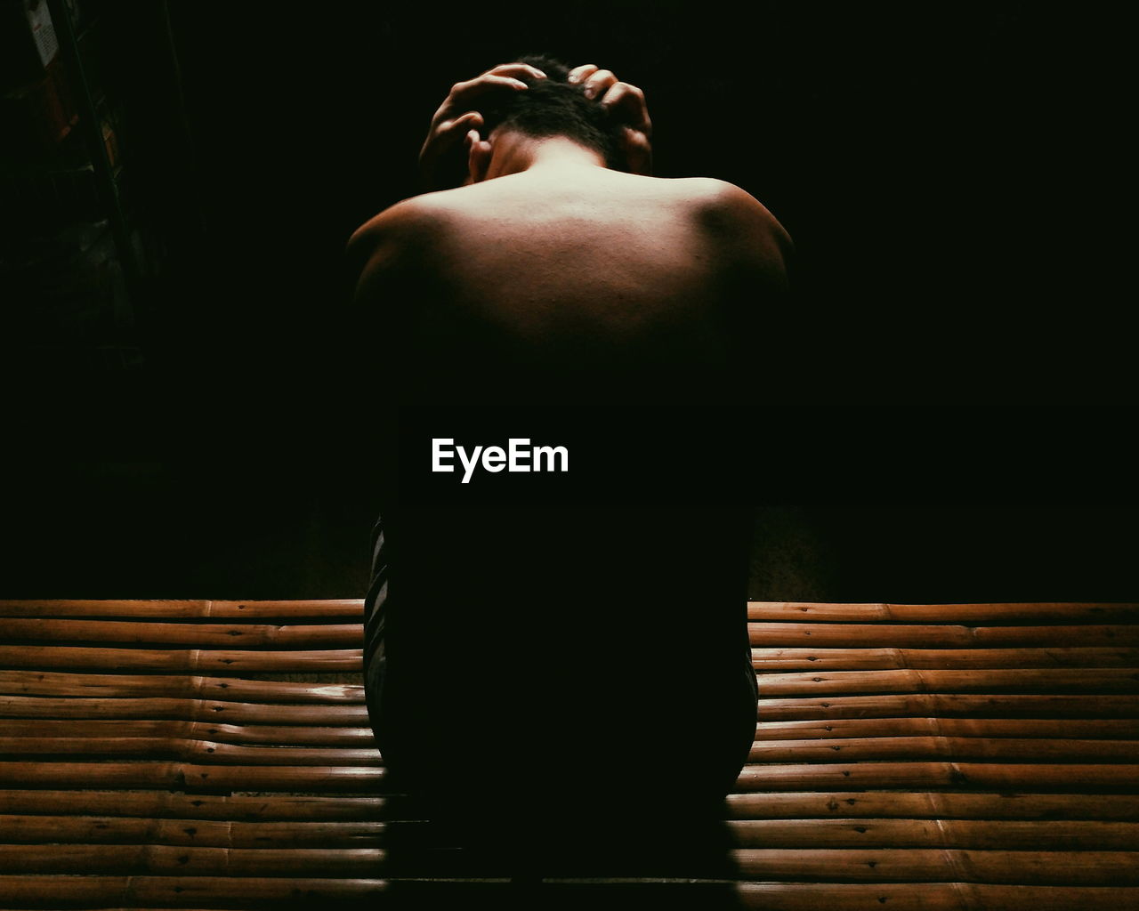 Rear view of shirtless depressed man sitting in darkroom