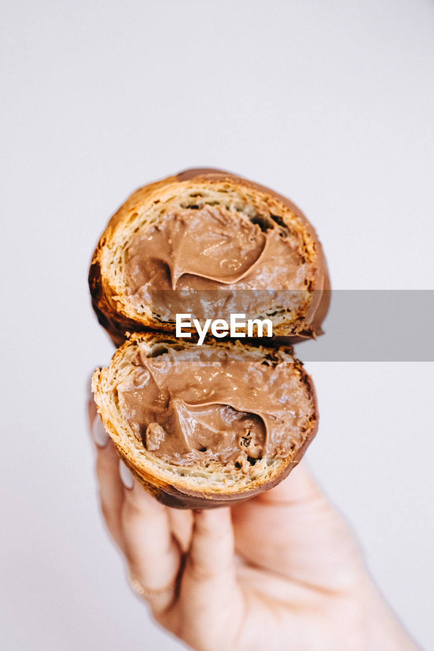 Close-up of hand holding croissant  worn chocolate over white background
