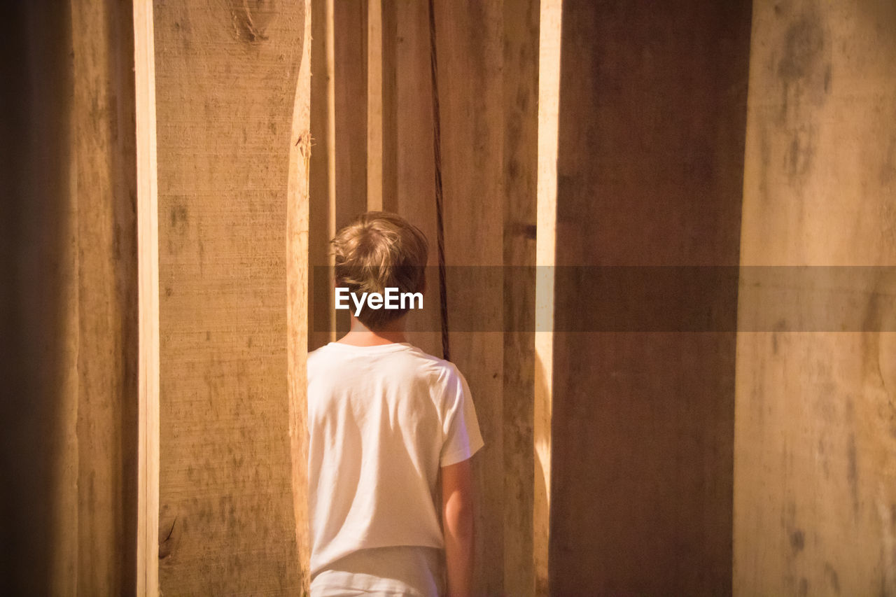 Rear view of boy standing amidst wooden planks