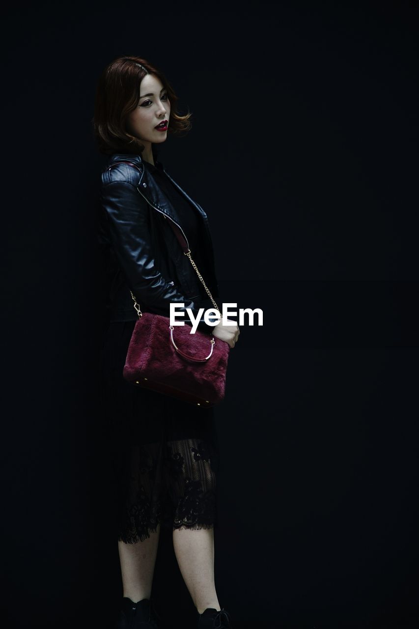 PORTRAIT OF YOUNG WOMAN STANDING OVER BLACK BACKGROUND