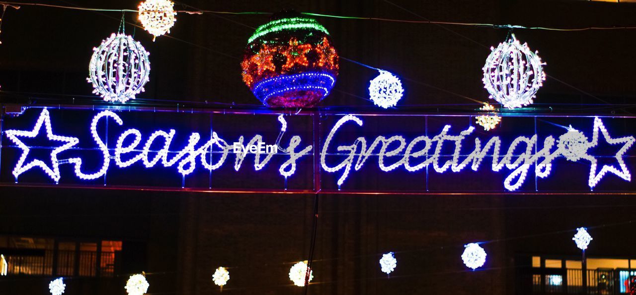 LOW ANGLE VIEW OF ILLUMINATED TEXT HANGING ON BLUE AT NIGHT