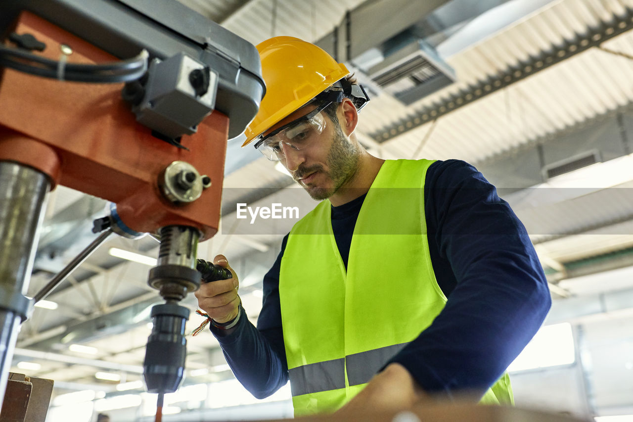 Worker operating drill in factory