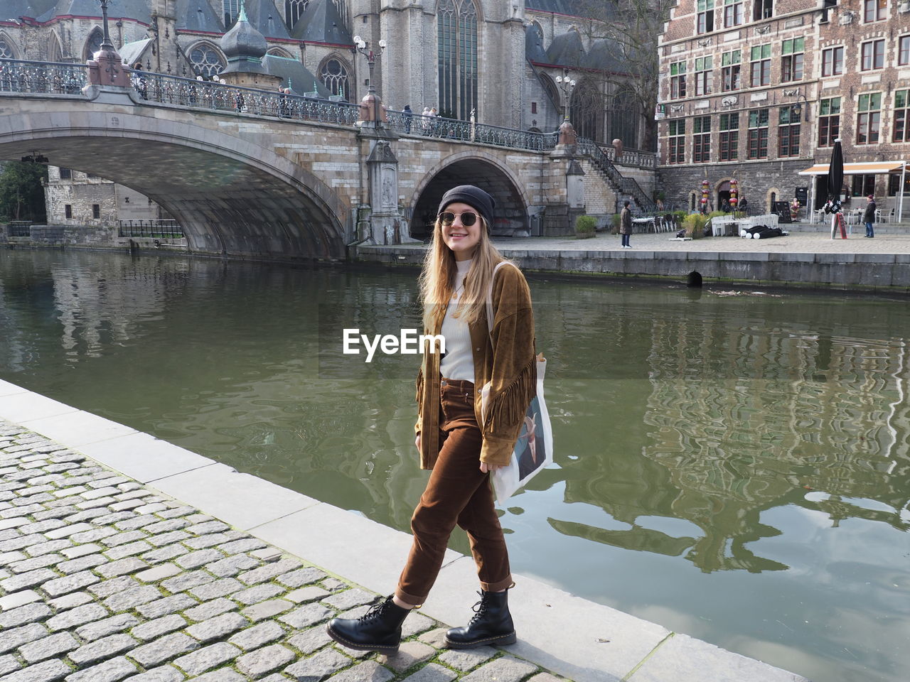 Portrait of young woman standing on bridge over canal